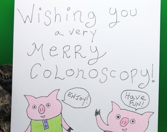 May include: A humorous greeting card with a hand-drawn illustration of two pink pigs. One pig is wearing a green dress with purple pockets and the other pig is wearing orange pants with a striped shirt. The card reads "Wishing you a very Merry Colonoscopy!" with one pig saying "Enjoy!" and the other saying "Have Fun!"