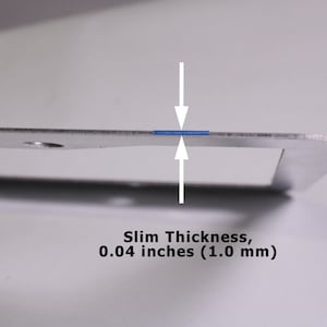 May include: A silver-colored metal frame with a slim thickness of 0.04 inches. The image features two white arrows pointing toward the edge of the frame, highlighting the measurement text Slim Thickness, 0.04 inches (1.0 mm) below the object.