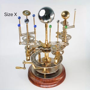 May include: A detailed brass and silver-toned model of the solar system, featuring planets, gears, and a wooden base. The model includes a large central sphere and smaller spheres representing planets, with the text "Size X" visible.