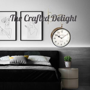 May include: A black double-sided wall clock with white face and gold accents. The clock has Roman numerals and the text "Village Clockmakers Co."