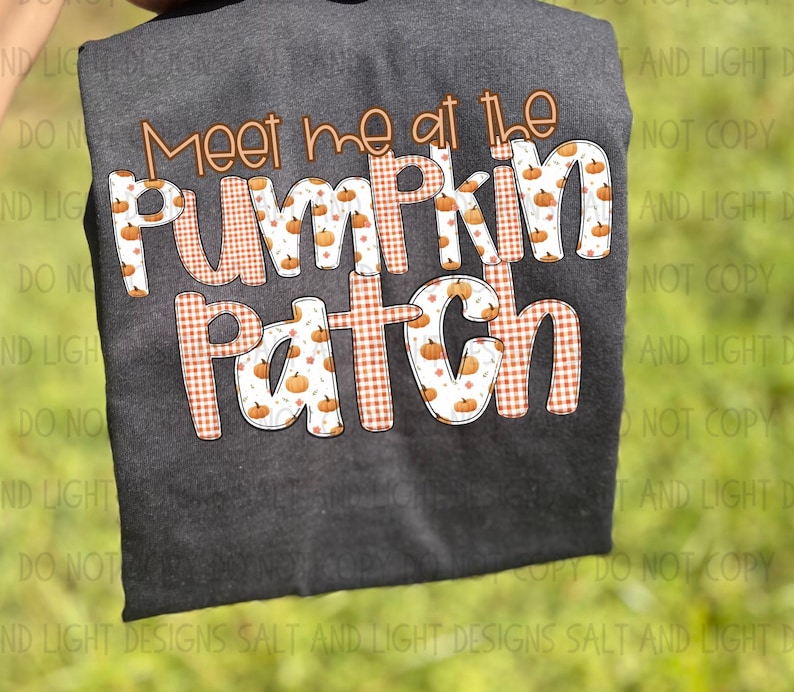May include: Dark gray sweatshirt with the text "Meet me at the Pumpkin Patch" in orange and white. The text has a pumpkin and plaid pattern. The sweatshirt is displayed against a green background.