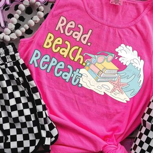 May include: A bright pink tank top with the words "Read. Beach. Repeat." in pastel colors. The graphic includes books, sunglasses, a starfish, and a wave. Black and white checkered shorts are visible on the left.