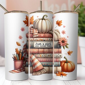 May include: White tumbler featuring a fall-themed design. The design includes a stack of books, pumpkins, autumn leaves, and a scarf. The text "Just a girl who loves fall" is printed on the books. A pencil holder with pencils is also visible.