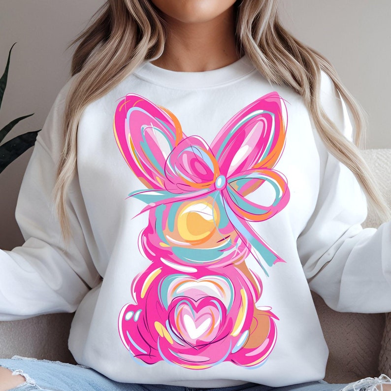 Peut inclure: Sweat-shirt blanc avec un motif de lapin abstrait rose et bleu. Le lapin a un grand n&oelig;ud rose et un c&oelig;ur au centre de sa poitrine.