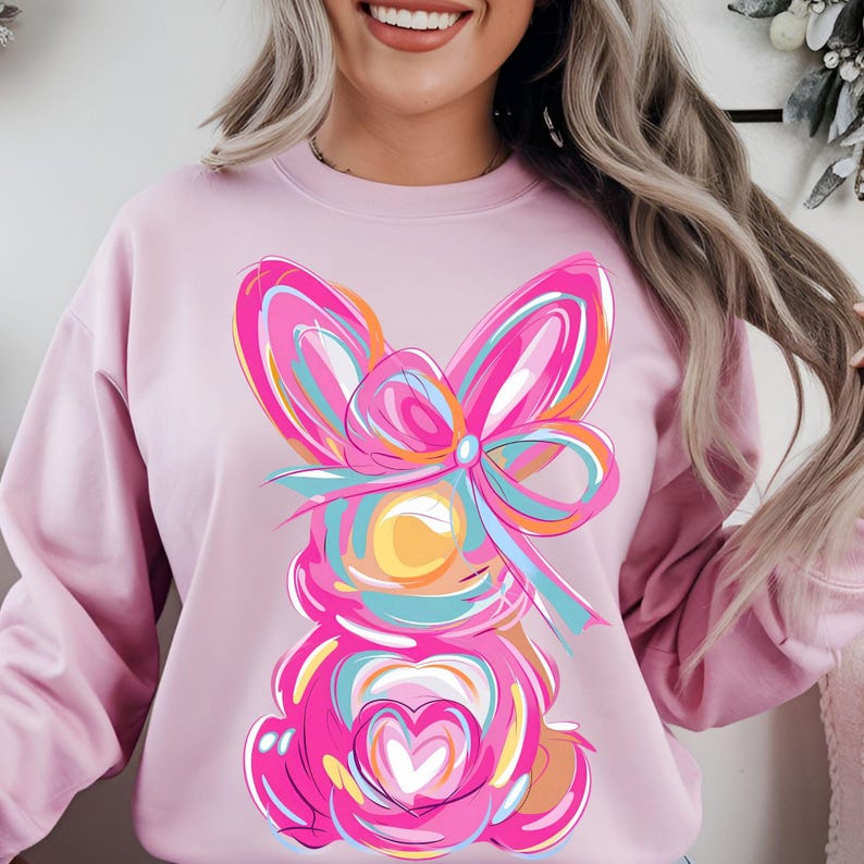 Peut inclure: Sweat-shirt rose avec un motif de lapin abstrait color&eacute;. Le lapin a un grand n&oelig;ud rose et un c&oelig;ur au centre.