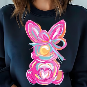 Peut inclure: Un sweat-shirt noir avec un lapin de dessin anim&eacute; rose et bleu avec un n&oelig;ud sur la t&ecirc;te. Le lapin tient un c&oelig;ur rose.