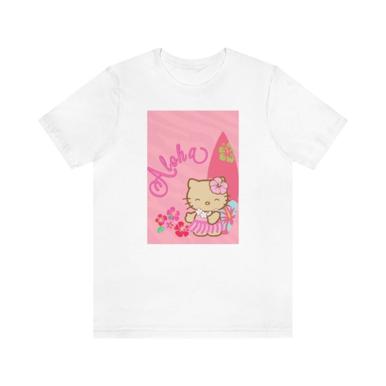 May include: White t-shirt featuring a pink graphic of Hello Kitty holding a surfboard and flowers. The graphic says "Aloha" in pink lettering.