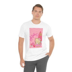 May include: White t-shirt featuring a pink graphic of Hello Kitty on a surfboard with the word "Aloha" in pink lettering.