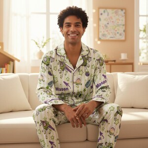 May include: A two-piece pajama set featuring a long-sleeved button-down shirt and matching pants. The fabric is white with light green vertical stripes, decorated with Buzz Lightyear graphics, green stars, and the name Mason printed in purple.