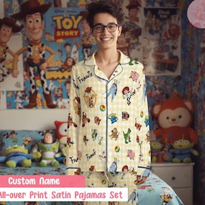 Può includere: Un completo pigiama in raso giallo con stampa all-over di personaggi di Toy Story. Il pigiama ha una camicia con bottoni con finiture blu navy e pantaloni abbinati. Il testo "Frankis" è stampato sulla camicia.