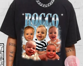 May include: Black t-shirt with a graphic of four babies with the word "ROCCO" in a blue and silver font.