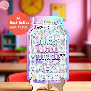 Puede incluir: Un letrero decorativo de madera en forma de tarro con el texto "Oliver's Magical Tooth Jar". El tarro está lleno de dientes de dibujos animados y se apoya en un soporte de madera. El letrero es en tonos de morado, azul y blanco. El soporte está incluido.