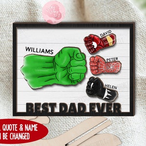 May include: Wooden sign with a green Hulk fist, red Iron Man fist, red and blue Spiderman fist, and a black Black Panther fist. The sign says "Best Dad Ever" and has the names "Williams", "David", "Peter", and "Helen" on it. The sign is on a white background.