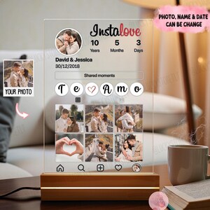 May include: A personalized acrylic photo display with a wooden base. The design features the text "Instalove" and "Te Amo", along with space for photos, names, and a date. The display is illuminated by a warm light.