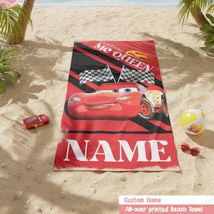 Może przedstawiać: Prostokątny ręcznik plażowy z grafiką czerwonego samochodu wyścigowego Lightning McQueen, czarnymi ukośnymi pasami i dwiema flagami w szachownicę. Napis Lightning McQueen oraz NAME wykonano białymi literami. Obok leży mały samochodzik i piłka.