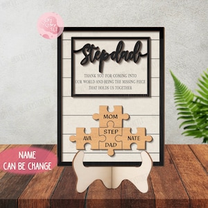 May include: A wooden Stepdad sign with a black frame and a white background with horizontal lines. The sign includes a puzzle with the words "Mom", "Step", "Dad", "Ava", and "Nate". The text reads "THANK YOU FOR COMING INTO OUR WORLD AND BEING THE MISSING PIECE THAT HOLDS US TOGETHER."