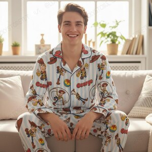 Puede incluir: Un conjunto de pijama de camisa de manga larga con botones y pantalón a juego, con un patrón de rayas verticales en azul claro y blanco. La tela está decorada con un estampado repetitivo del personaje Woody de Toy Story, sombreros y pelotas.