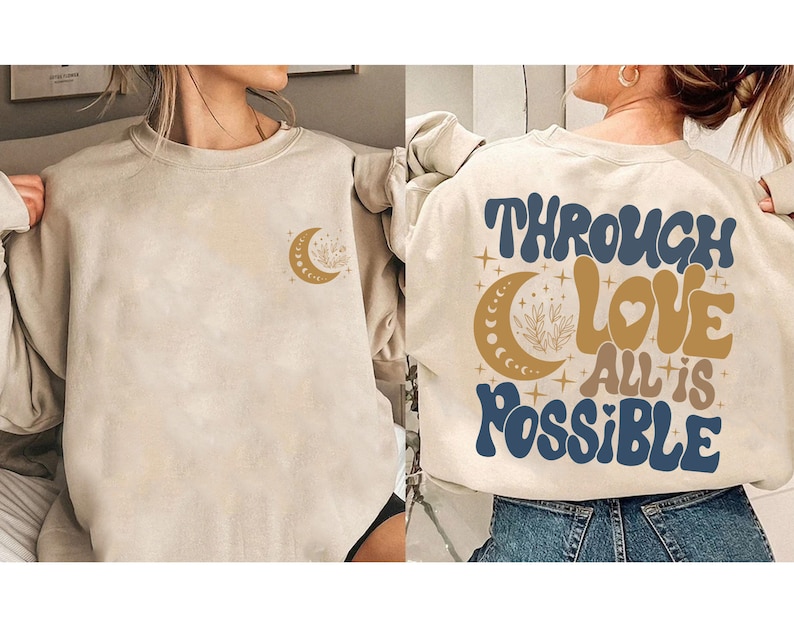 May include: A beige sweatshirt with a crescent moon and stars design on the front and the text "Through Love All is Possible" in blue and gold lettering on the back.