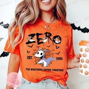 May include: Orange t-shirt featuring the word "ZERO" with a graphic of Zero from "The Nightmare Before Christmas." The design includes bats, a spiderweb, and the text "EST. 1993." The shirt is a short-sleeved crew neck.
