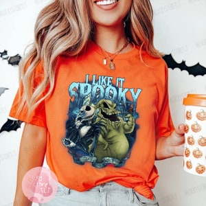 May include: Orange t-shirt featuring a graphic of Jack Skellington and Oogie Boogie from The Nightmare Before Christmas, with the text "I Like It Spooky". The design is in shades of blue, green, and black.