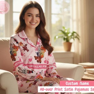 K&ouml;nnte beinhalten: Rosa Satin-Pyjama-Set mit Allover-Print von Zeichentrickfiguren und Herzen. Das Pyjama-Oberteil hat eine Knopfleiste und einen Reverskragen. Die passende Hose vervollst&auml;ndigt das Set. Der Text auf dem Pyjama lautet "MITCHELL & EMILY NCHE" und "Custom Name".