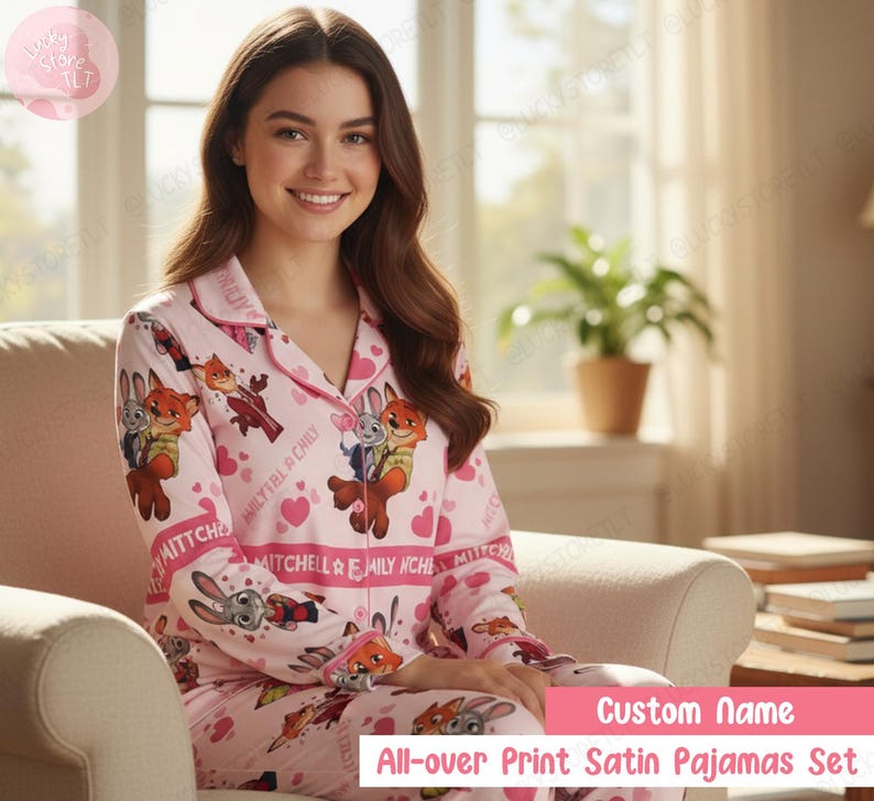 K&ouml;nnte beinhalten: Rosa Satin-Pyjama-Set mit Allover-Print von Zeichentrickfiguren und Herzen. Das Pyjama-Oberteil hat eine Knopfleiste und einen Reverskragen. Die passende Hose vervollst&auml;ndigt das Set. Der Text auf dem Pyjama lautet "MITCHELL & EMILY NCHE" und "Custom Name".