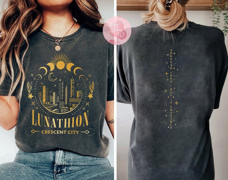 May include: Black t-shirt with a gold graphic of a crescent moon, stars, and a cityscape with the text "Lunathion Crescent City". The back of the shirt has gold text that reads "Through Love, All Is Possible".