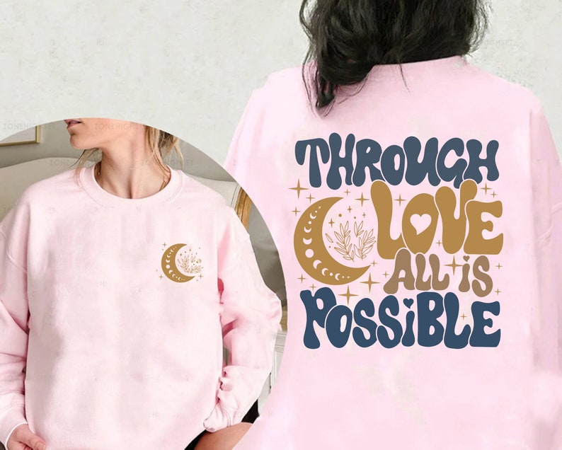 May include: Pink sweatshirt with the text "Through Love All is Possible" in blue and gold lettering with a crescent moon and stars. The front of the sweatshirt has a smaller crescent moon with stars in gold.