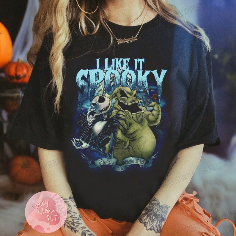 May include: Black t-shirt featuring a graphic of Jack Skellington and Oogie Boogie from The Nightmare Before Christmas. The text "I Like It Spooky" is displayed above the characters. The shirt is a Halloween-themed apparel item.