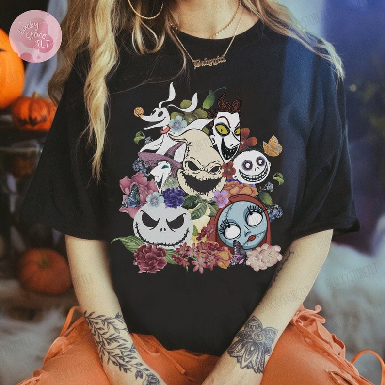 May include: Black t-shirt featuring a colorful graphic of characters from "The Nightmare Before Christmas" surrounded by flowers and butterflies. The design includes Jack Skellington, Sally, and other iconic characters.