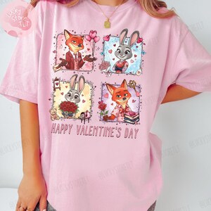 Pu&ograve; includere: T-shirt rosa chiaro con una grafica colorata di volpi e conigli dei cartoni animati in cornici a tema San Valentino. Il testo "HAPPY VALENTINE'S DAY" &egrave; stampato in bianco sotto. La maglietta ha maniche corte.