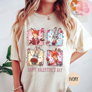 Pu&ograve; includere: T-shirt color avorio con una grafica colorata con volpi e conigli dei cartoni animati in cornici quadrate. Il design include cuori, fiori e la scritta "HAPPY VALENTINE'S DAY". La maglietta ha girocollo e maniche corte.