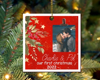 Könnte beinhalten: Roter und goldener Weihnachtsbaumschmuck mit einem Foto eines sich küssenden Paares. Der Anhänger trägt den Text "Charlie & Pol unser erstes Weihnachten 2022".