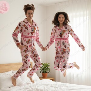 K&ouml;nnte beinhalten: Passende rosa Pyjamas mit Zeichentrickfiguren und Herzen. Die Pyjamas haben lange &Auml;rmel und Hosen. Der Text "CARLY MITCHELL" ist auf Brust und &Auml;rmeln aufgedruckt. Zwei Personen springen auf einem Bett.