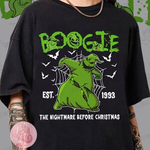 May include: Black t-shirt featuring a green graphic of Oogie Boogie from "The Nightmare Before Christmas." The design includes the word "BOOGIE" in green, the year "1993," and the phrase "THE NIGHTMARE BEFORE CHRISTMAS."