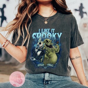 May include: Dark gray t-shirt featuring a graphic of Jack Skellington and Oogie Boogie from The Nightmare Before Christmas, with the text "I Like It Spooky". The design is in shades of blue, green, and white.
