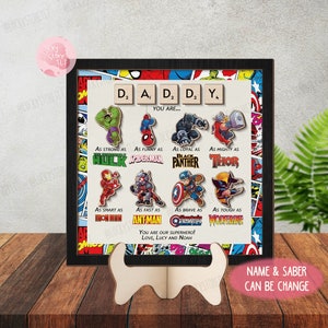 May include: A framed print with a comic book theme featuring a collage of Marvel superhero characters. The print includes the words "D.A.D.D.Y. You are..." and a message that reads "You are our superhero! Love, Lucy and Noah".