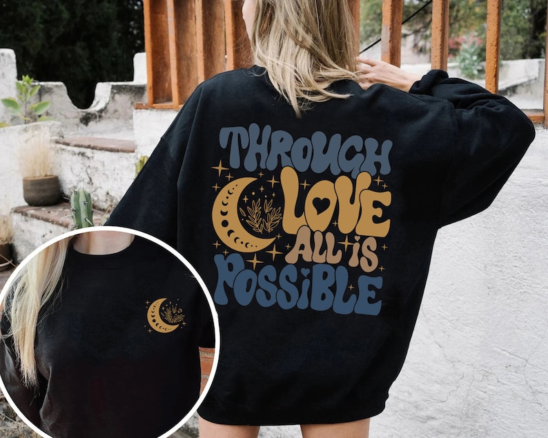 May include: Black sweatshirt with a graphic design featuring a crescent moon, stars, and the text "Through Love All is Possible".