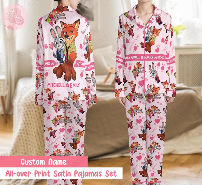 K&ouml;nnte beinhalten: Rosa Satin-Pyjama-Set mit einem sich wiederholenden Muster aus Zeichentrickfiguren, Herzen und dem Text "MITCHELL EMILY". Das lang&auml;rmlige Oberteil und die Hose enthalten eine gro&szlig;e Grafik eines Fuchses und eines Hasen. Der Text "Custom Name" und "All-over Print Satin Pajamas Set" sind ebenfalls sichtbar.