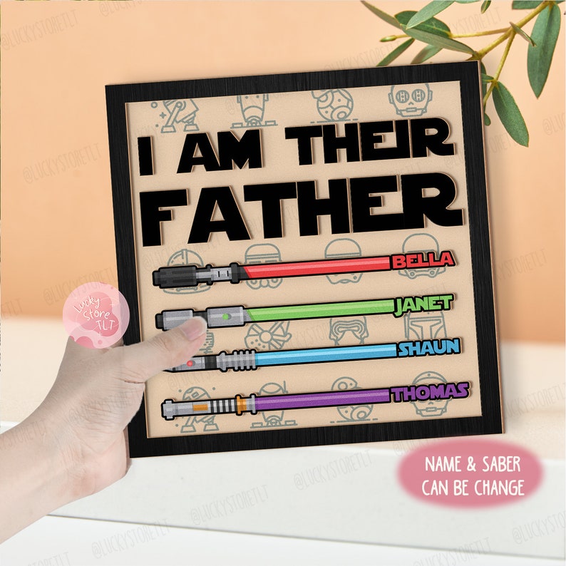 Pode incluir: Uma placa de madeira com moldura preta e o texto "Eu sou o pai deles" em letras pretas. A placa tem um tema de Star Wars com sabres de luz e personagens dos filmes. Os nomes Bella, Janet, Shaun e Thomas est&atilde;o listados abaixo dos sabres de luz.