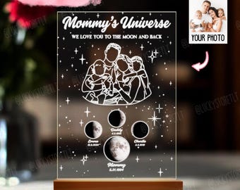 May include: A white acrylic light-up sign with a wood base. The sign features a family silhouette with the text "Mommy's Universe" and "We love you to the moon and back". The sign also includes a moon phase design with names and dates.