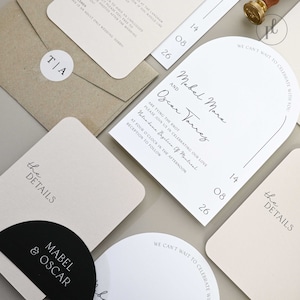 May include: Wedding invitation suite with a modern arch design. The invitation features the names "Mabel Mara" and "Oscar Torres" in elegant script. The details card features a black and white circle with the names "Mabel & Oscar" in a minimalist font.