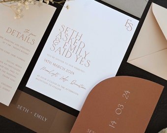 May include: A wedding invitation suite with a white background and brown accents. The invitation features the text "Seth asked & Emily said yes" in a modern font. The date of the wedding is listed as "14th March 2024" and the location is "Moonlight Ledge, Queenstown".