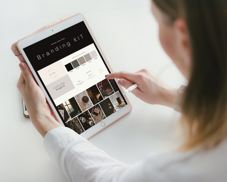 May include: A person is using a tablet displaying a "Branding Kit" layout. The screen shows a logo design, color palette, and sample images. The tablet is held in a light-colored case, and a stylus is used to interact with the screen.