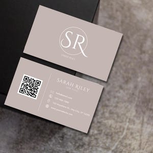 May include: A beige business card with a white circle containing the letters "SR" and the text "SARAH RILEY" below. The card also includes contact information, a QR code, and a website address.