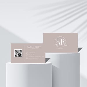 May include: A light brown business card with a QR code on the left side and text that reads "SARAH RILEY YOUR LIFE" on the right side. The other side of the card is light brown with a white circle containing the letters "SR" and the text "SARAH RILEY" below.