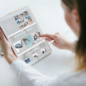 May include: A woman uses a stylus to scroll through a tablet screen displaying a website with a light gray background. The website features a section titled "Recent Photos & Projects" with images of a car, a palm tree, and a beach. Another section titled "Recent Videos" displays thumbnails of videos.