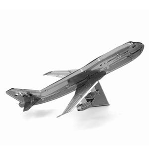 May include: A silver-colored metal model airplane, a Boeing 747, is displayed on a white background. The model is detailed with wings, tail, and a stand. The airplane is angled upwards, suggesting flight.