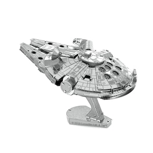 Puede incluir: Modelo metálico plateado de la nave espacial Halcón Milenario. El modelo presenta detalles intrincados, con paneles y elementos circulares. Está montado sobre un soporte con el texto "© 2013 Lucasfilm Ltd. & TM."