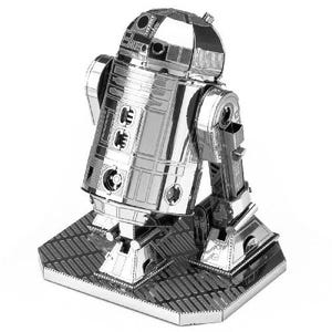 May include: A silver metal model of the Star Wars droid R2-D2. The model is constructed from interlocking metal sheets and stands on a rectangular base. The droid's iconic dome head and cylindrical body are clearly visible, showcasing intricate details.